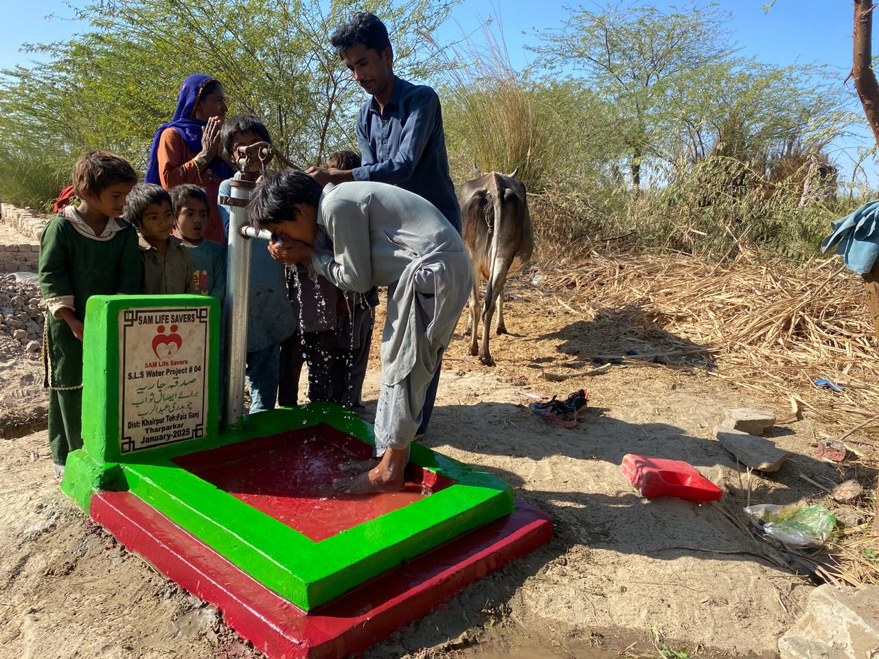 A newly installed blue water hand pump by SAM Life Savers, surrounded by local villagers and children celebrating access to clean drinking water in the arid region of Tharparkar.